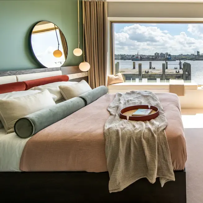 Made-up double bed with a round mirror and river view